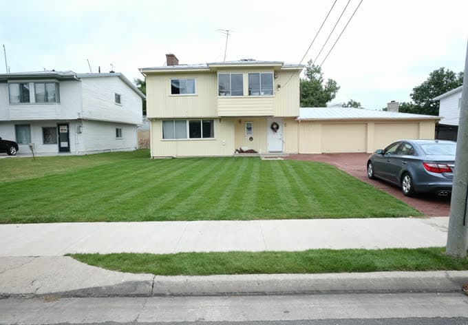 Pelouse avant tondue en bandes régulières devant une maison à deux étages